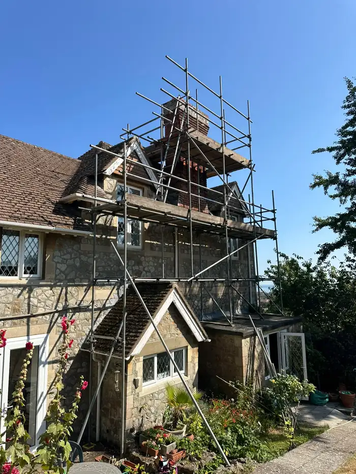 Scaffold around a chimney stack on a stone house in Hythe during repointing by JH Roofing