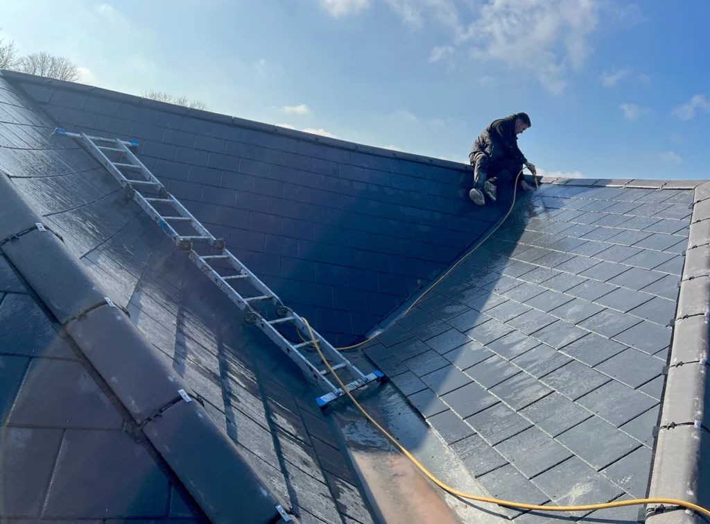Roofer repairing tiled pitched roof using ladders and harness